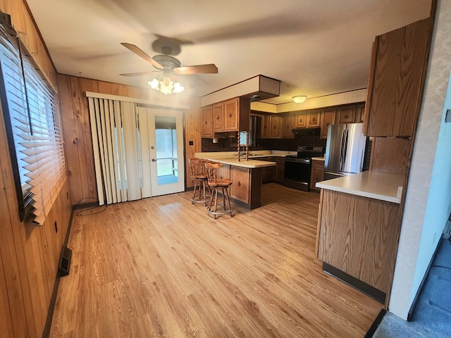 kitchen with a center island, light hardwood / wood-style flooring, wooden walls, a kitchen breakfast bar, and stainless steel appliances