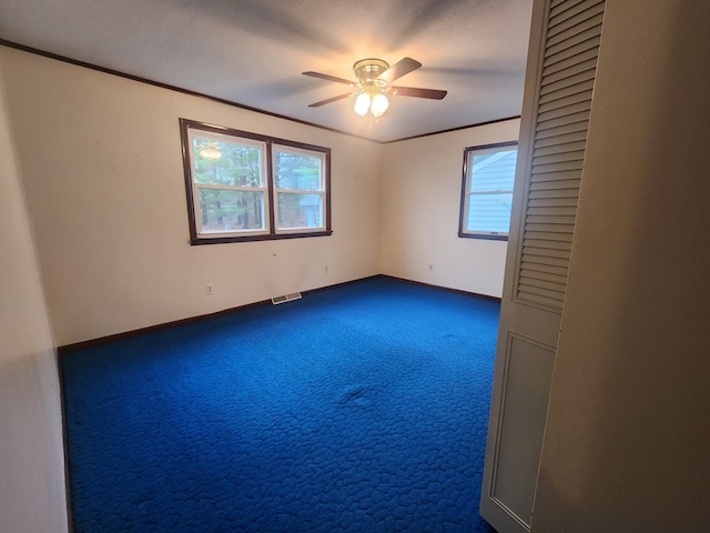 empty room featuring dark colored carpet, ornamental molding, and ceiling fan