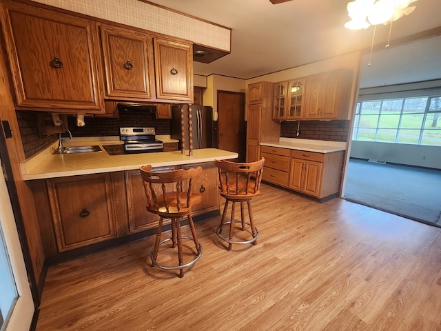 kitchen with sink, light hardwood / wood-style flooring, appliances with stainless steel finishes, a kitchen breakfast bar, and kitchen peninsula