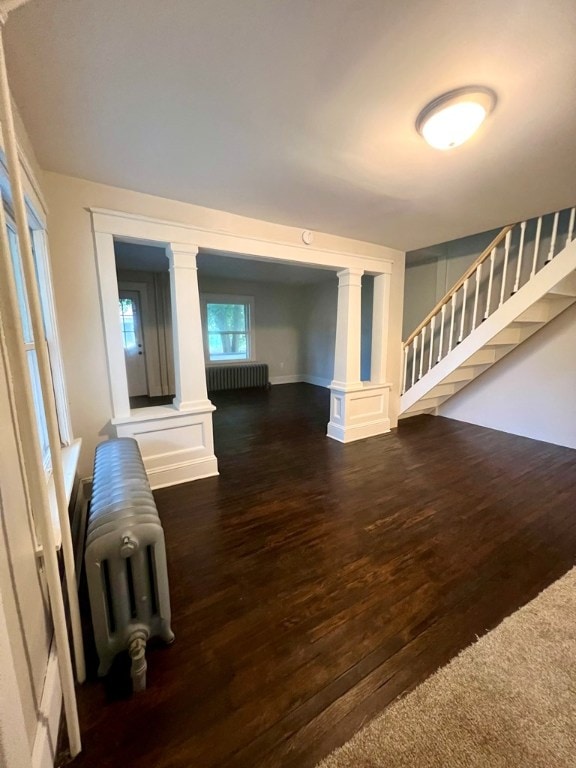 unfurnished living room featuring dark wood-type flooring, radiator heating unit, and ornate columns