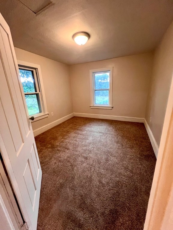 empty room with a healthy amount of sunlight, dark carpet, and a textured ceiling