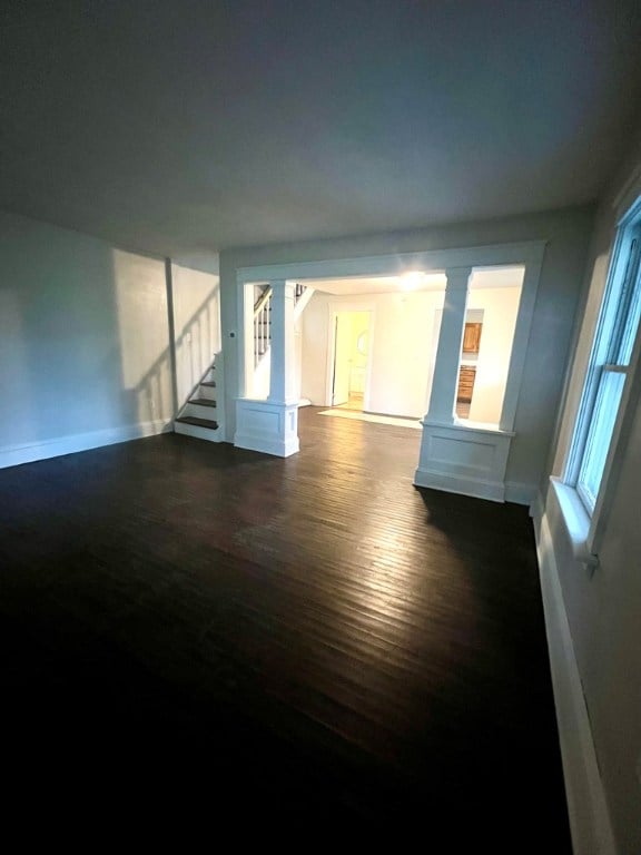 unfurnished living room featuring ornate columns and dark hardwood / wood-style flooring