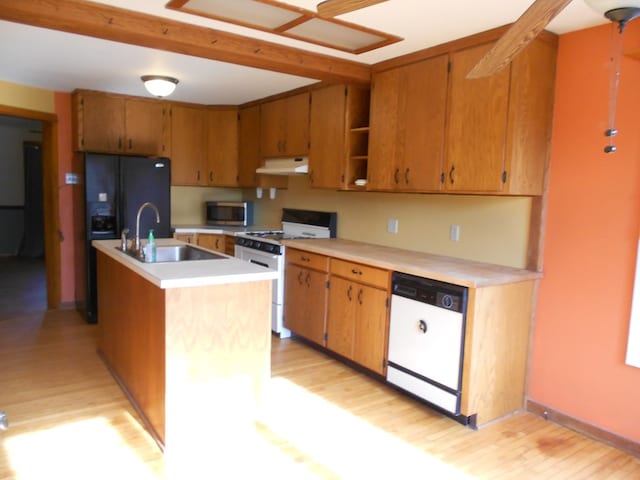 kitchen featuring sink, white appliances, light hardwood / wood-style floors, and an island with sink