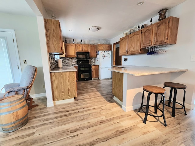 kitchen featuring sink, light hardwood / wood-style flooring, kitchen peninsula, decorative backsplash, and black appliances