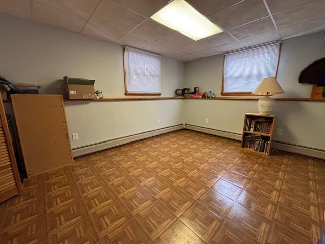 basement featuring parquet floors, a drop ceiling, and baseboard heating