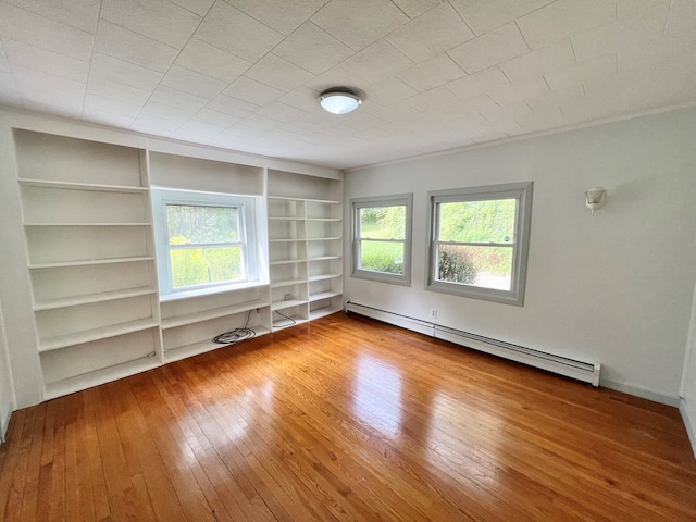 unfurnished room featuring a wealth of natural light, a baseboard radiator, built in shelves, and wood-type flooring