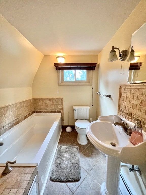 bathroom with a bathing tub, vaulted ceiling, a baseboard radiator, tile patterned flooring, and toilet