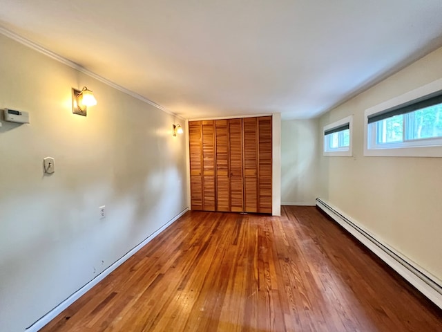 unfurnished bedroom with hardwood / wood-style floors, crown molding, a baseboard radiator, and a closet