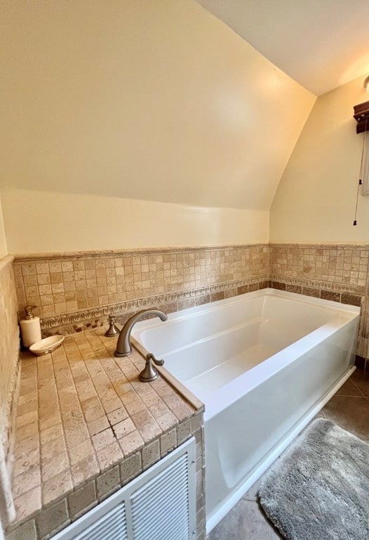 bathroom with lofted ceiling, tile patterned flooring, and a bathing tub