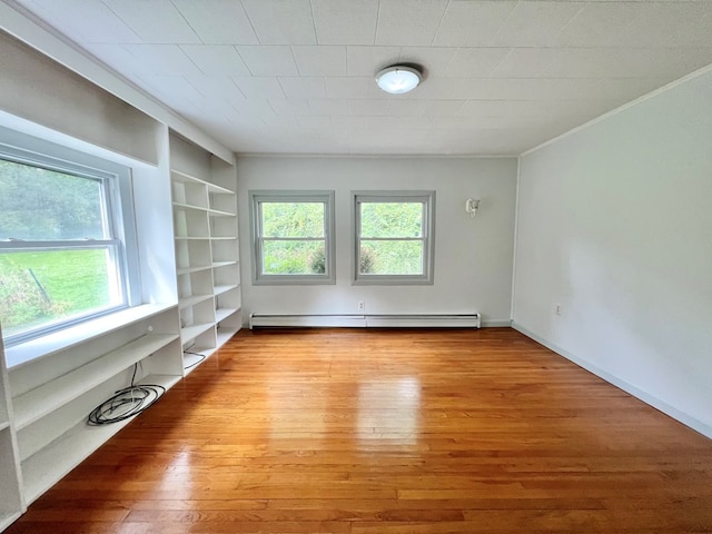 empty room with a baseboard heating unit, built in features, and light wood-type flooring