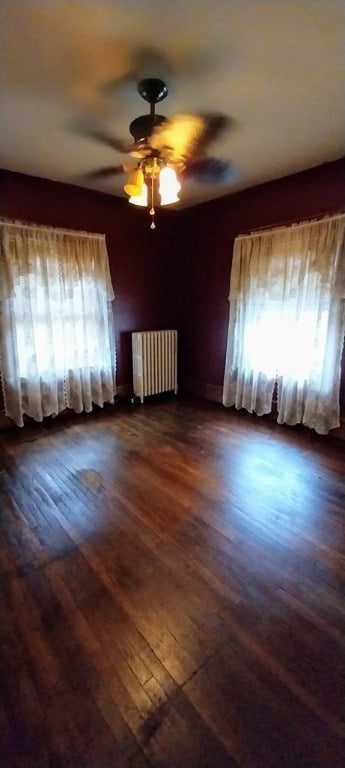 empty room with dark wood-type flooring, ceiling fan, and radiator