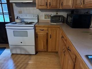 kitchen featuring backsplash, white electric range oven, range hood, and light wood-type flooring