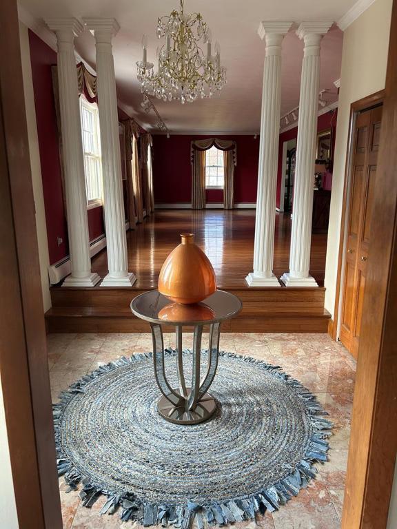 hallway featuring baseboard heating, crown molding, a chandelier, and ornate columns