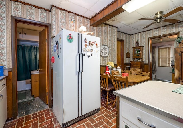 kitchen featuring white refrigerator, ceiling fan, white cabinetry, and a drop ceiling