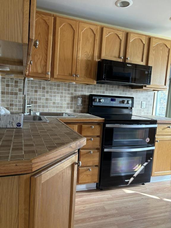 kitchen featuring tile counters, backsplash, light hardwood / wood-style floors, and black appliances