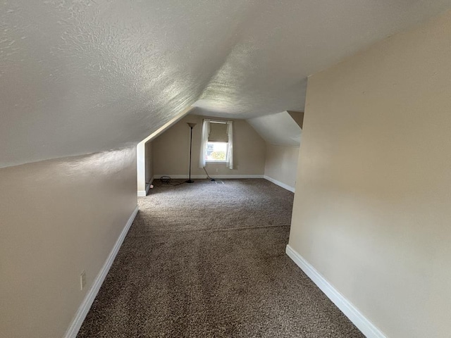 additional living space featuring lofted ceiling, a textured ceiling, and dark colored carpet