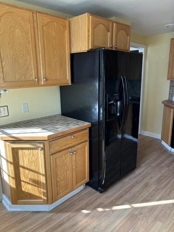 kitchen featuring tile counters, black fridge with ice dispenser, and light wood-type flooring