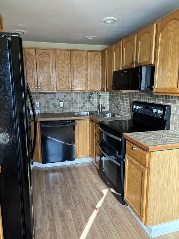 kitchen with light wood-type flooring, sink, tasteful backsplash, and black appliances