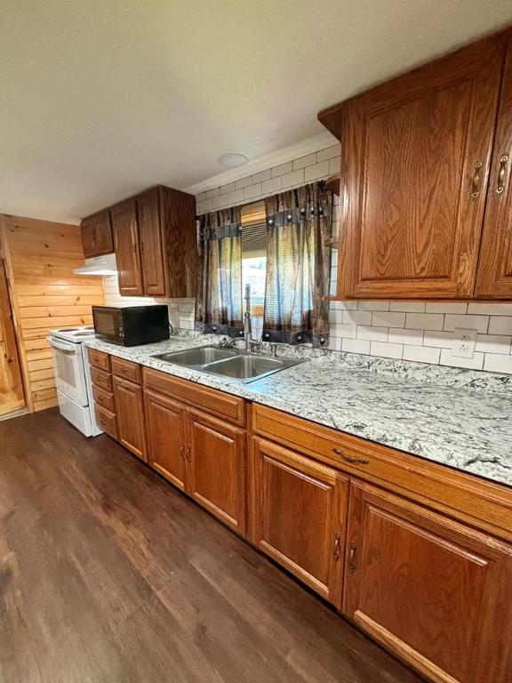 kitchen with sink, backsplash, wooden walls, dark hardwood / wood-style floors, and light stone counters