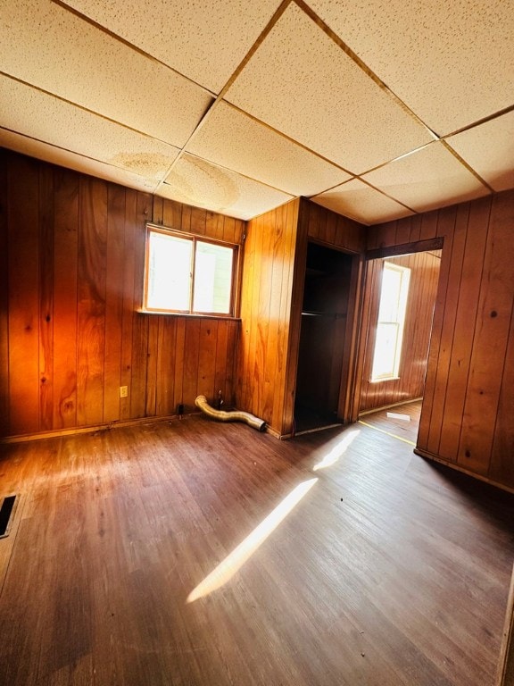 unfurnished room featuring wood-type flooring, a paneled ceiling, and wooden walls