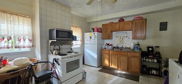 kitchen with sink, white appliances, light tile patterned floors, ceiling fan, and a textured ceiling