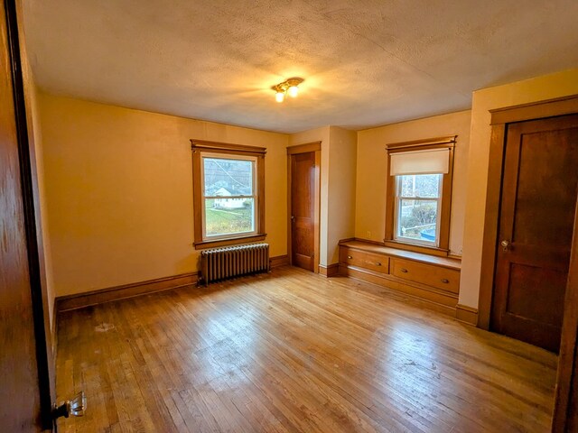 unfurnished bedroom with multiple windows, radiator, a textured ceiling, and light hardwood / wood-style floors