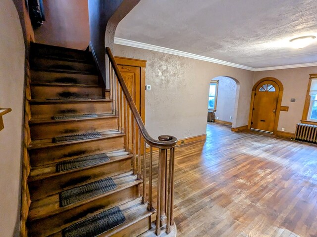 stairway with hardwood / wood-style floors, crown molding, radiator heating unit, and a textured ceiling