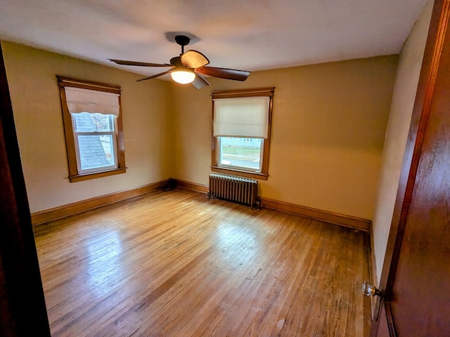 empty room featuring light wood-type flooring, radiator, ceiling fan, and baseboards