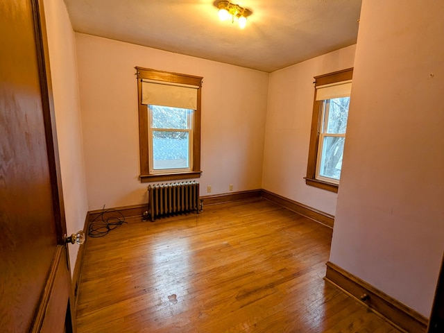 spare room featuring baseboards, radiator heating unit, and wood finished floors