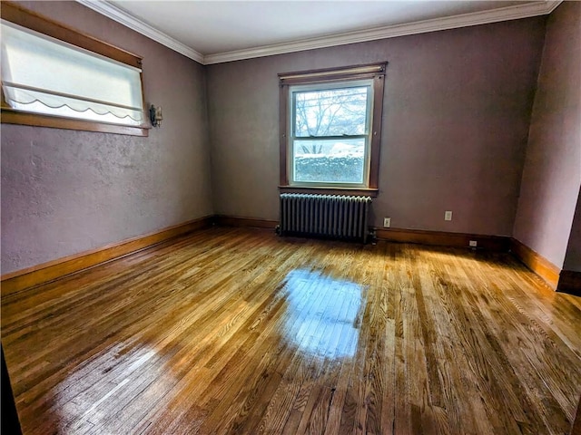 spare room featuring light wood-type flooring, radiator heating unit, baseboards, and crown molding