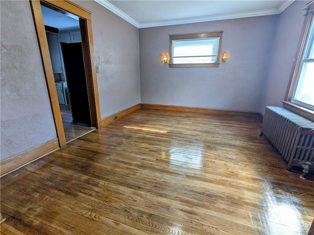 spare room with radiator, a healthy amount of sunlight, crown molding, and wood finished floors