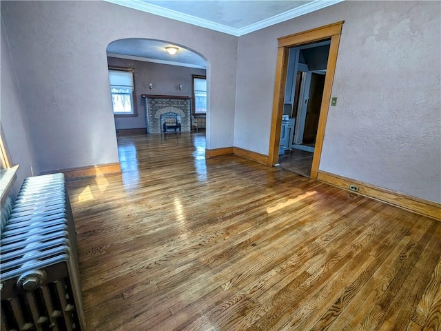 unfurnished living room featuring baseboards, arched walkways, wood finished floors, crown molding, and a fireplace