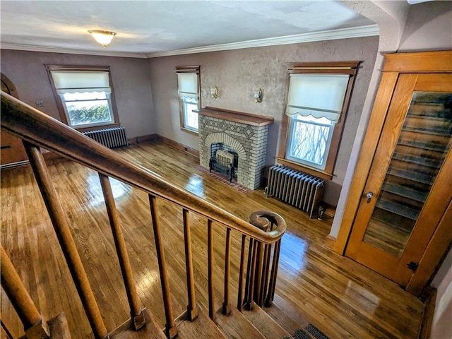 stairway with crown molding, radiator, a fireplace, and wood finished floors