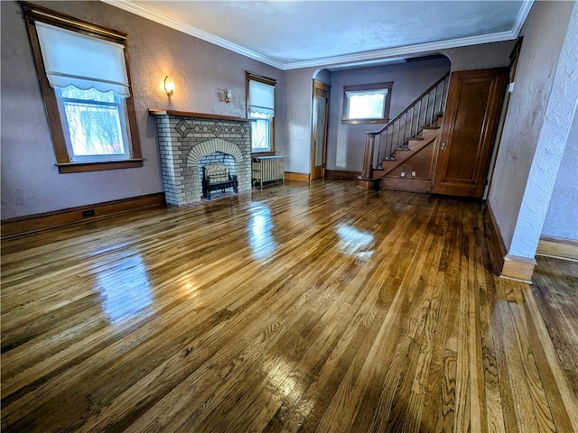 unfurnished living room with stairway, arched walkways, wood finished floors, and ornamental molding