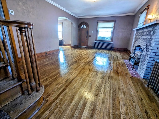 unfurnished living room with plenty of natural light, a brick fireplace, crown molding, and radiator heating unit