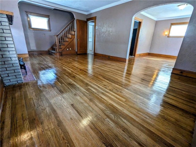 unfurnished living room with ornamental molding, arched walkways, light wood-style flooring, and stairs