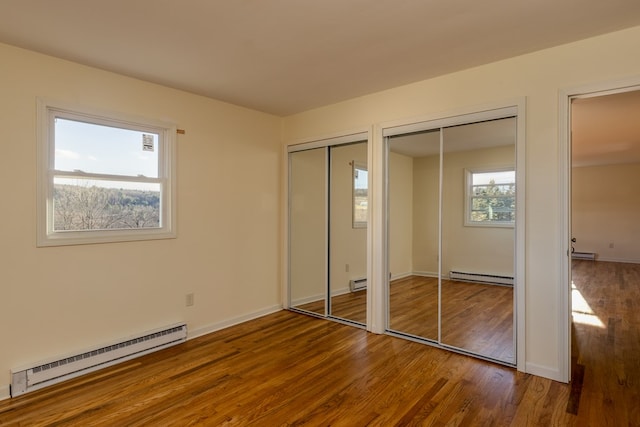 unfurnished bedroom with baseboard heating, hardwood / wood-style floors, and two closets