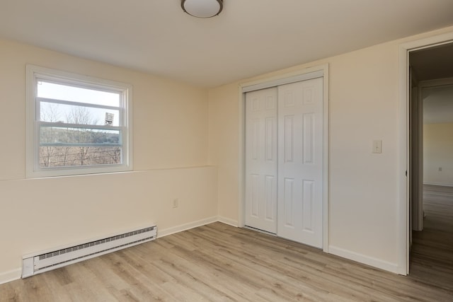 unfurnished bedroom featuring baseboard heating, a closet, and light wood-type flooring