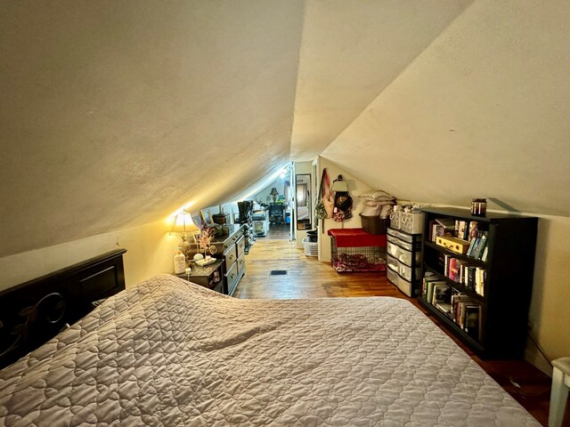 bedroom with wood-type flooring, vaulted ceiling, and a textured ceiling