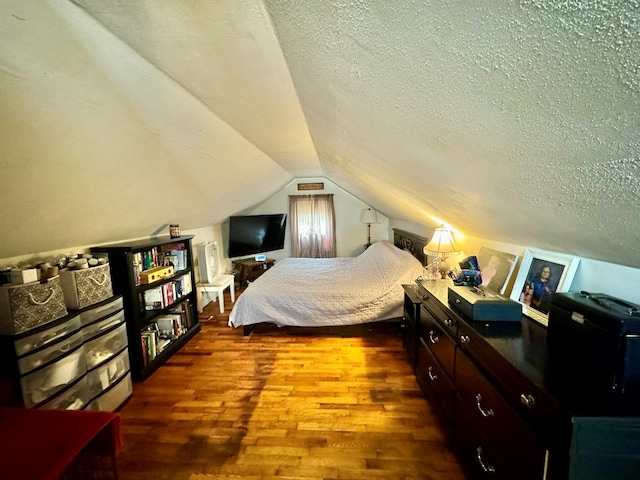 bedroom featuring wood-type flooring, vaulted ceiling, and a textured ceiling