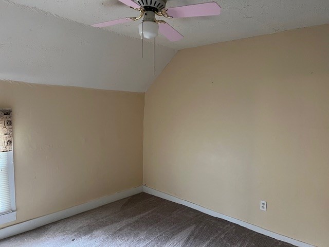 additional living space featuring dark carpet, ceiling fan, vaulted ceiling, and a textured ceiling