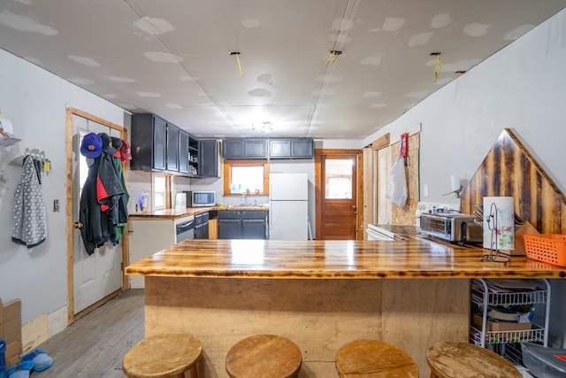 kitchen with a breakfast bar area, wooden counters, white refrigerator, kitchen peninsula, and light hardwood / wood-style floors