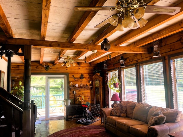 living room featuring wood walls, beamed ceiling, a wood stove, ceiling fan, and wooden ceiling