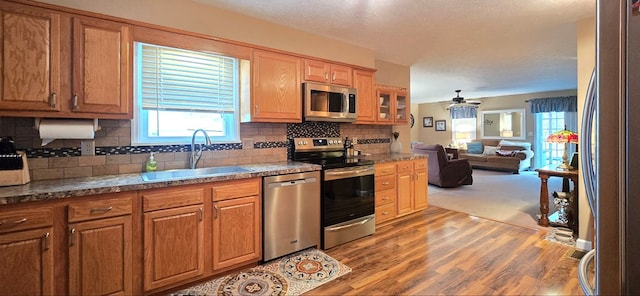 kitchen with appliances with stainless steel finishes, sink, backsplash, ceiling fan, and light hardwood / wood-style flooring