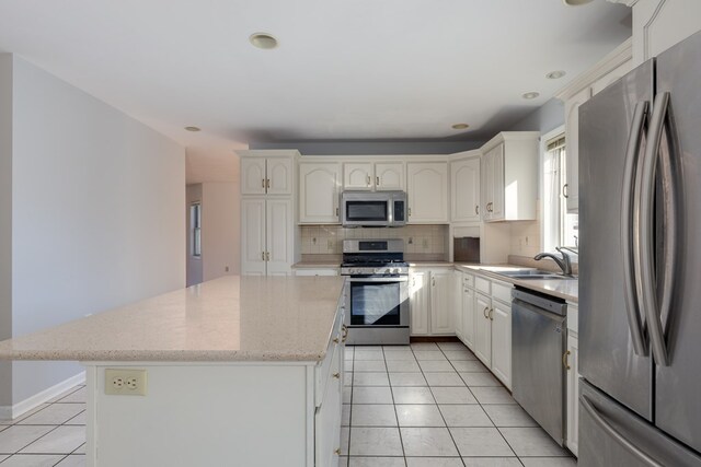 kitchen with light tile patterned flooring, a kitchen island, appliances with stainless steel finishes, white cabinetry, and sink