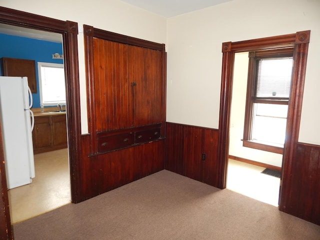 unfurnished bedroom with sink, carpet floors, wood walls, and white fridge