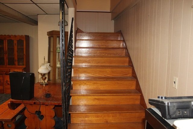 stairway with wood walls and a drop ceiling