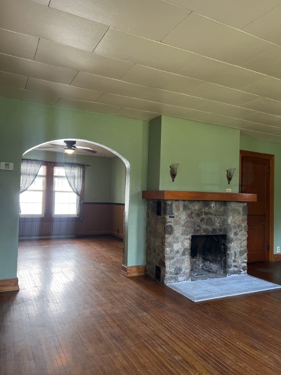 unfurnished living room featuring a stone fireplace, ceiling fan, and hardwood / wood-style flooring