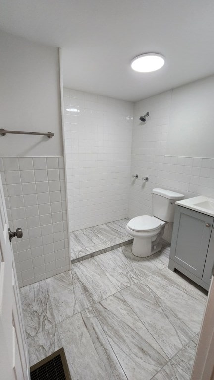 bathroom featuring tiled shower, vanity, toilet, and tile walls