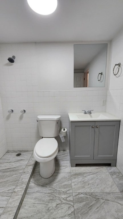 bathroom featuring vanity, a tile shower, tile walls, and toilet